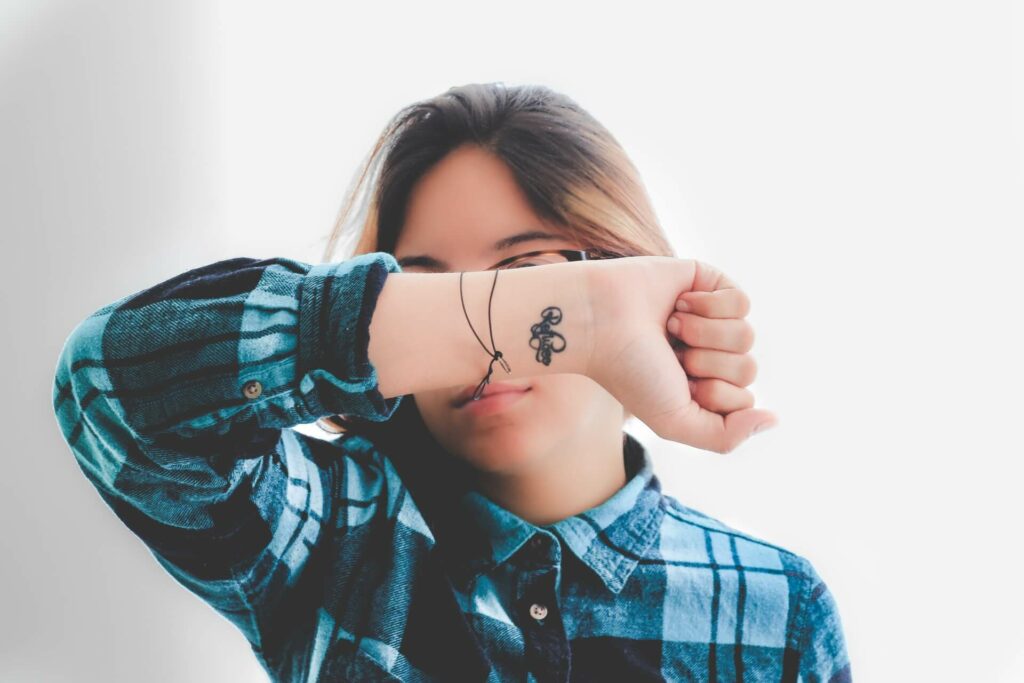 A woman with a tattoo on her hand hides her face