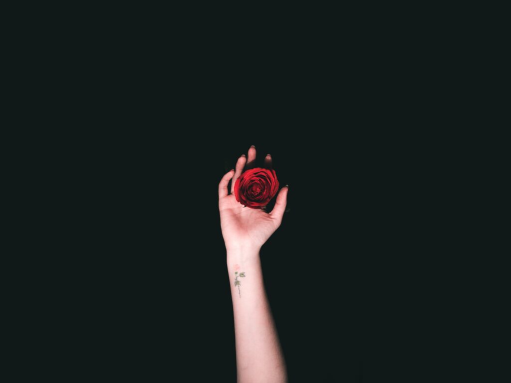 A woman with a tattoo on her hand holding a red rose in her hand