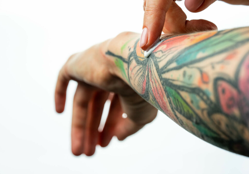 Female tattooed hands hold a jar of cream. Fingers