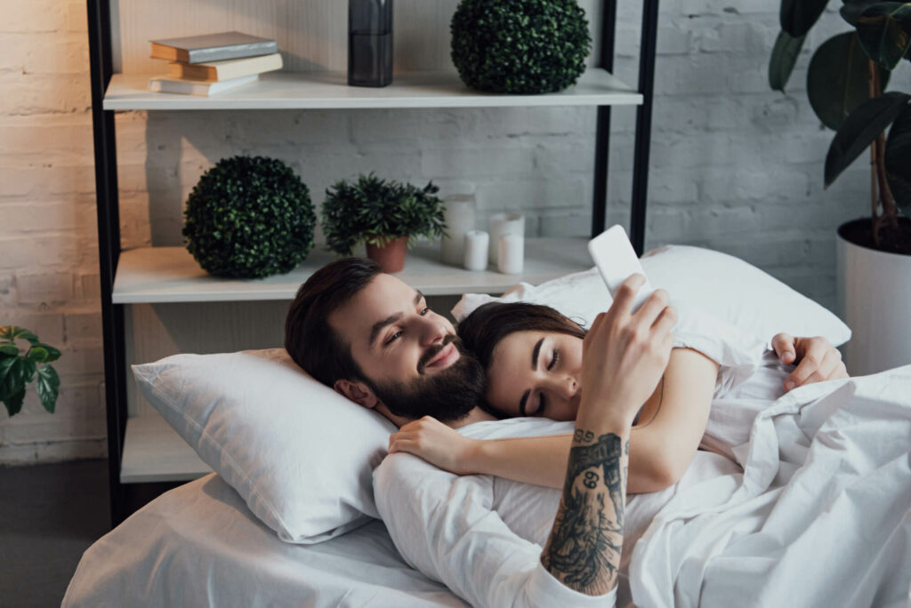 Handsome man using smartphone while woman sleeping in bad